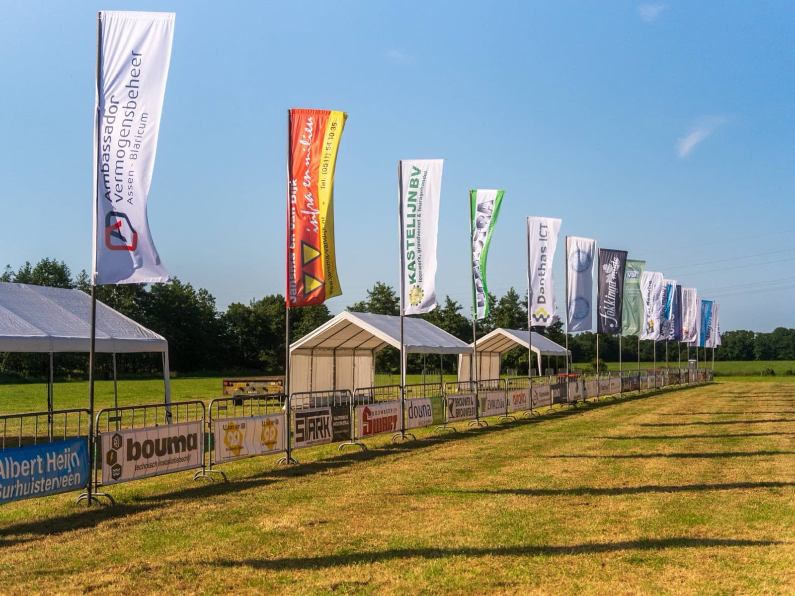 Rij baniervlaggen en bedrukte dranghekdoeken van sponsoren langs het parcours