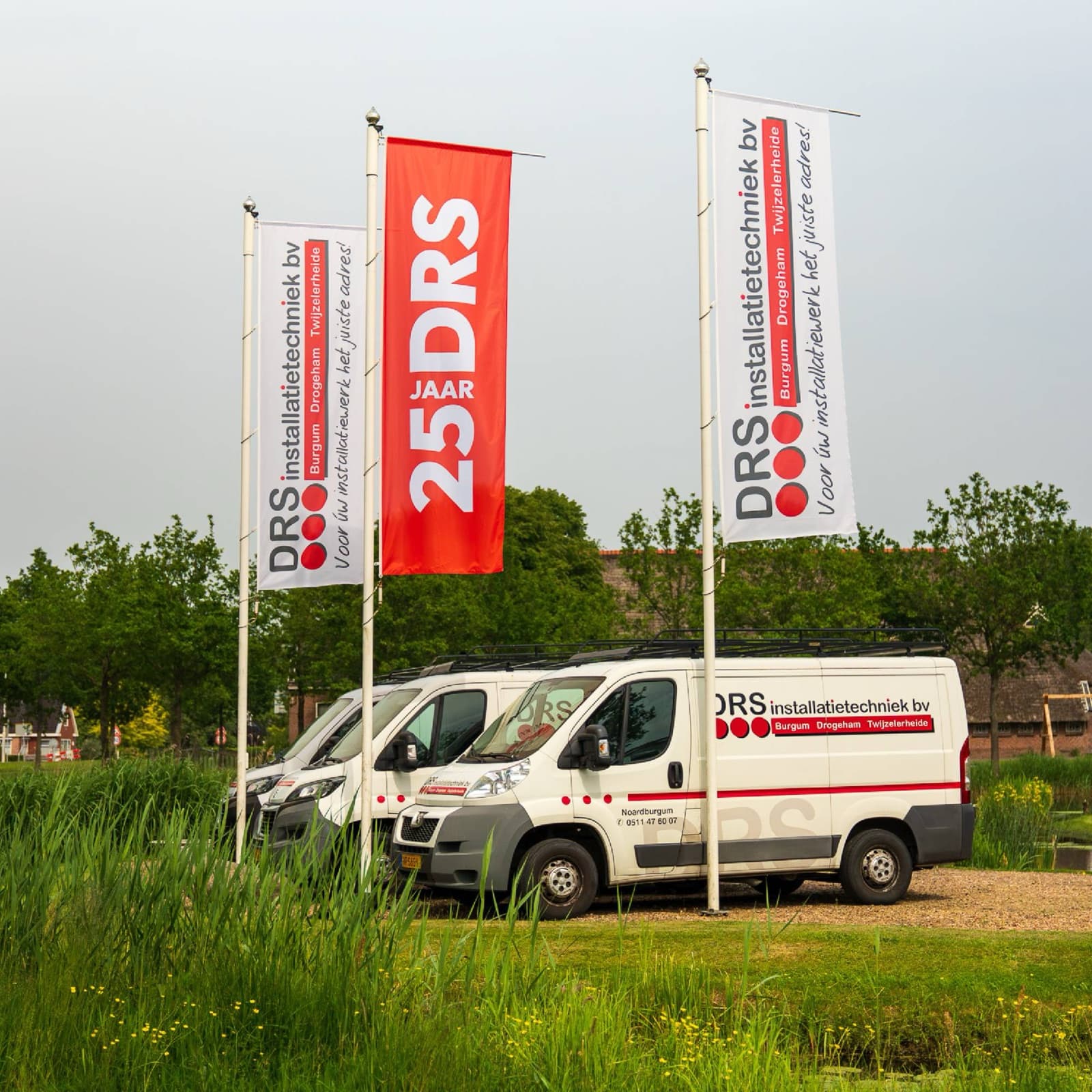 Baniervlaggen van DRS en de 25 jaar-jubileumvlag boven de bedrijfsbusjes