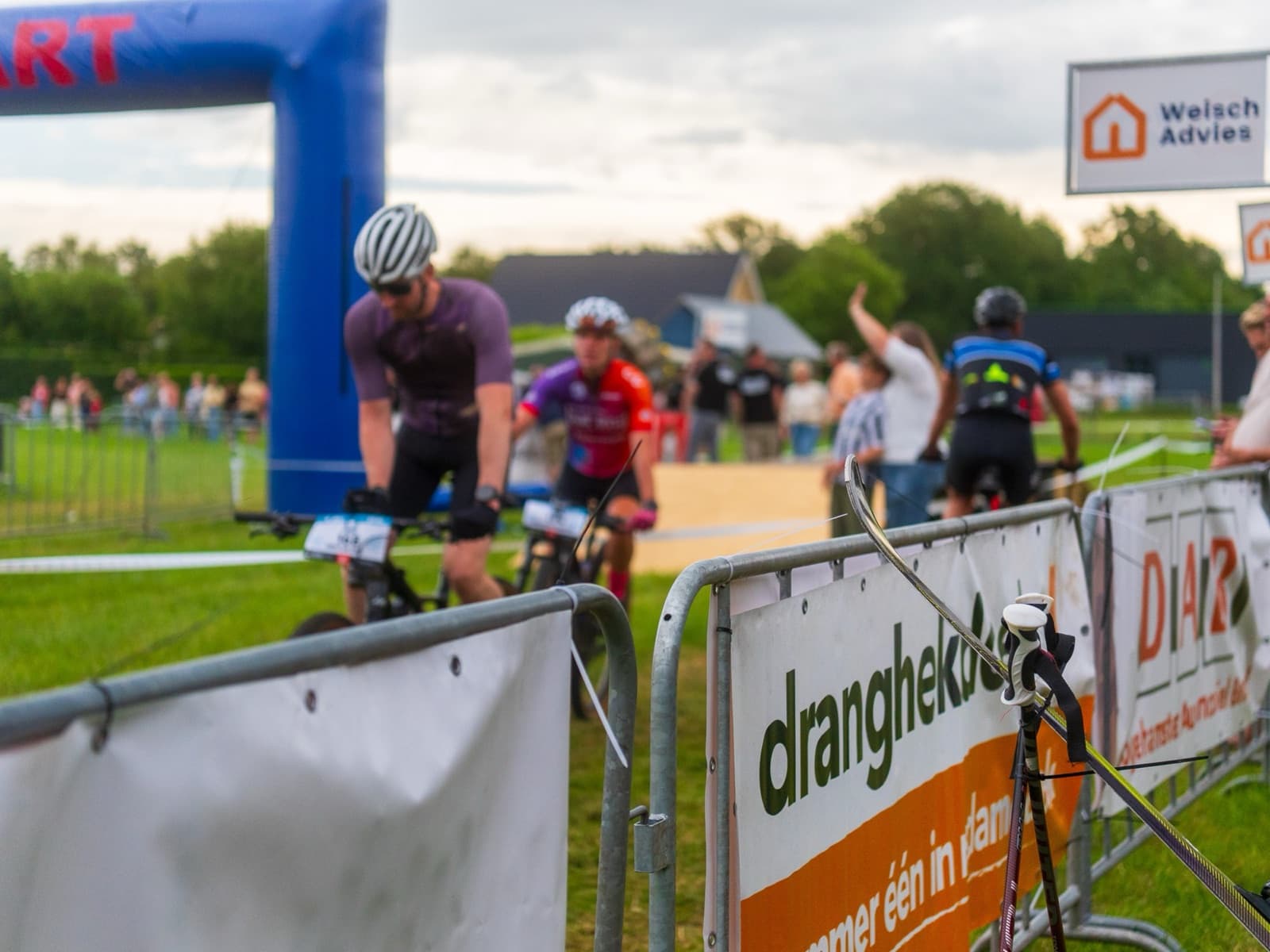 Mountainbikers bij de finish, langs dranghekdoeken van sponsoren