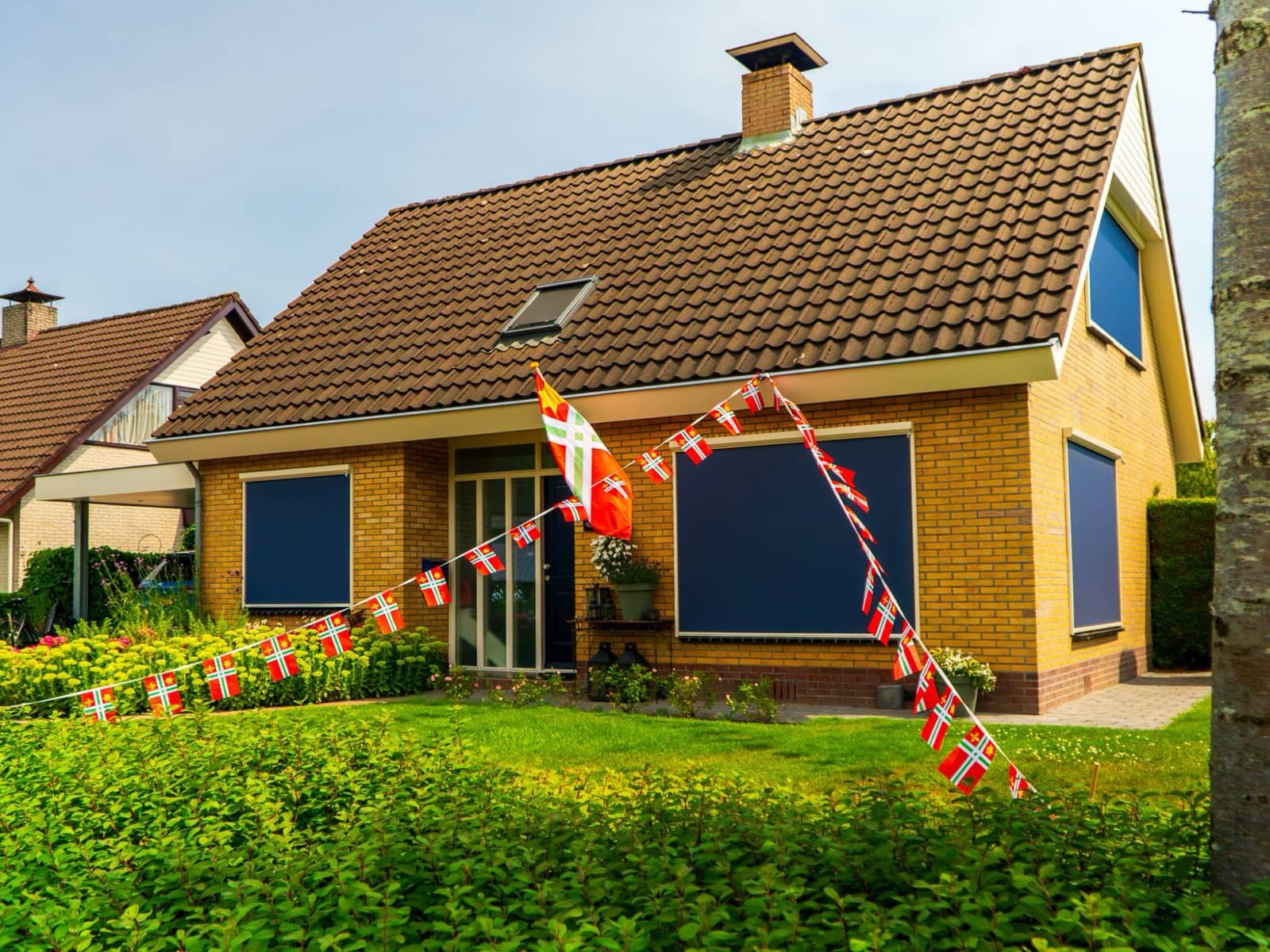 De Dorpsvlag Buitenpost als gevelvlag aan een huis, met Dorpsvlag-vlaggenlijnen in de voortuin