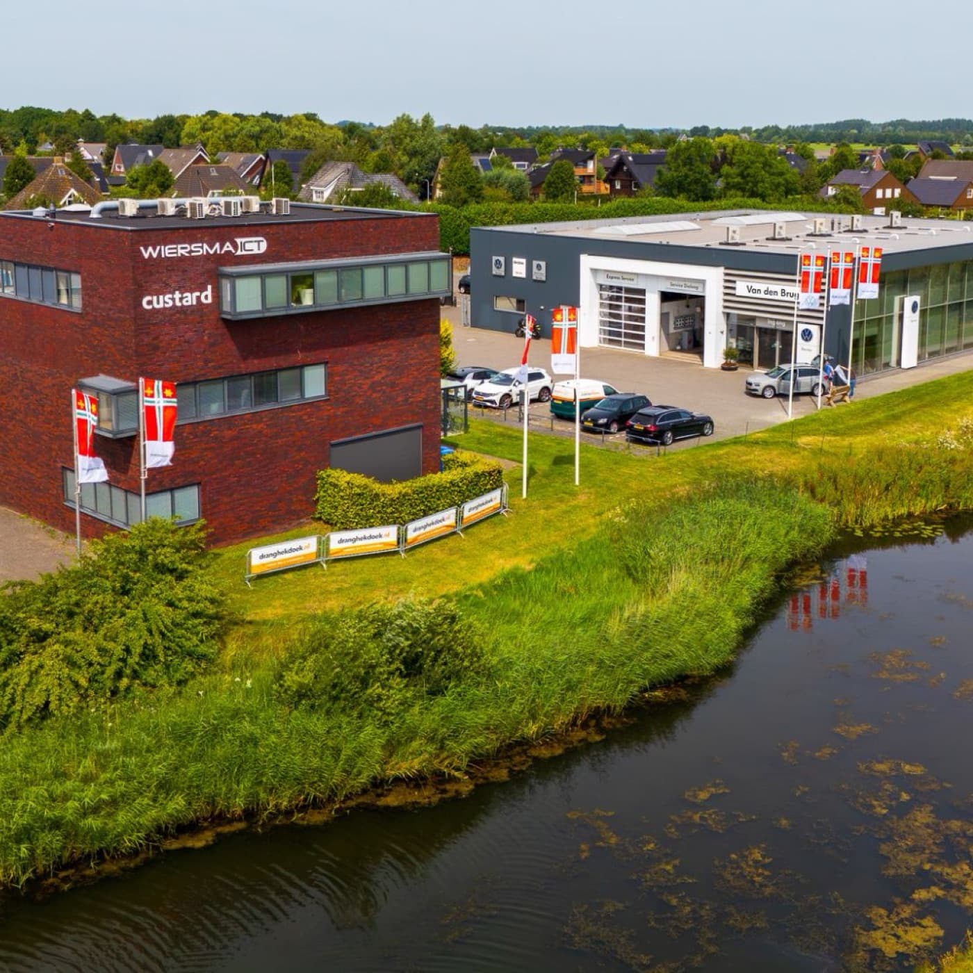 Luchtfoto van bedrijven in Buitenpost met Dorpsvlaggen aan de masten en dranghekdoeken van Dranghekdoek.nl
